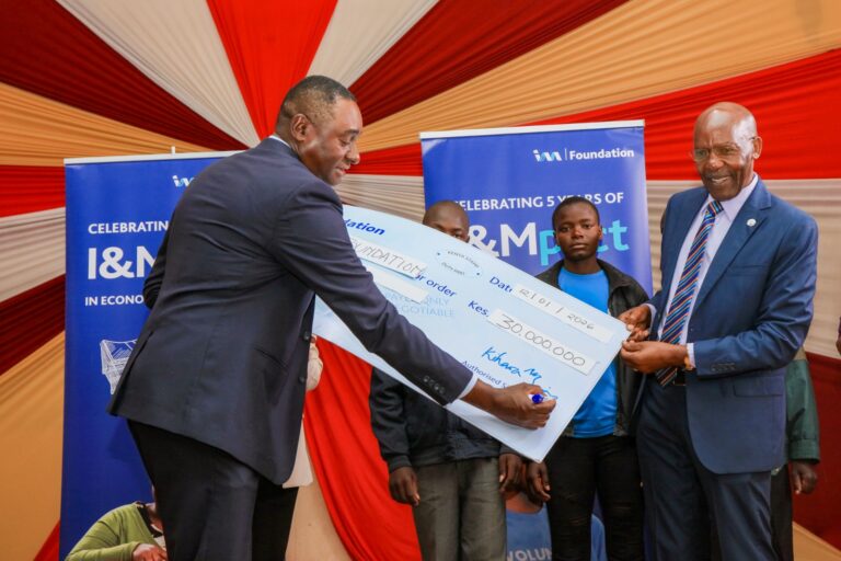 I&M Bank Regional CEO Kihara Maina signs a dummy cheque during the I&M Bank,I&M Foundation and Palmhouse Foundation Senior School Sendoff Partnership at Holy Family Basilica. Looking on is Palmhouse Foundation Managing Director and Founder Eric.
